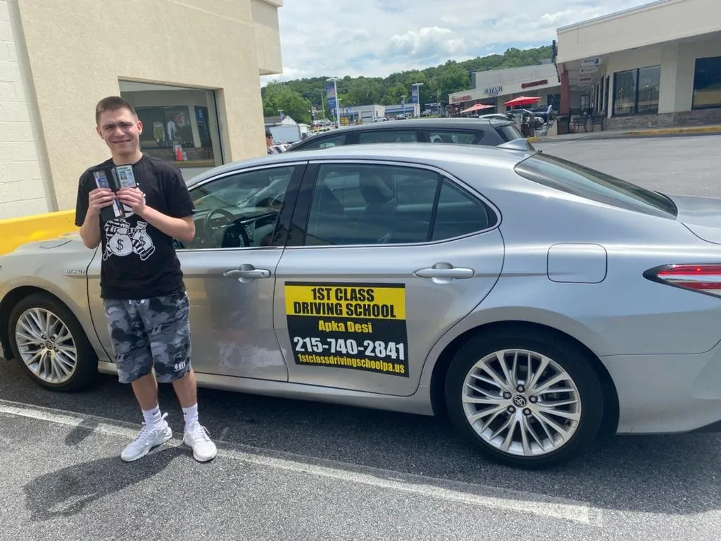 Teen student holding his paperwork next to the silver driving-school car